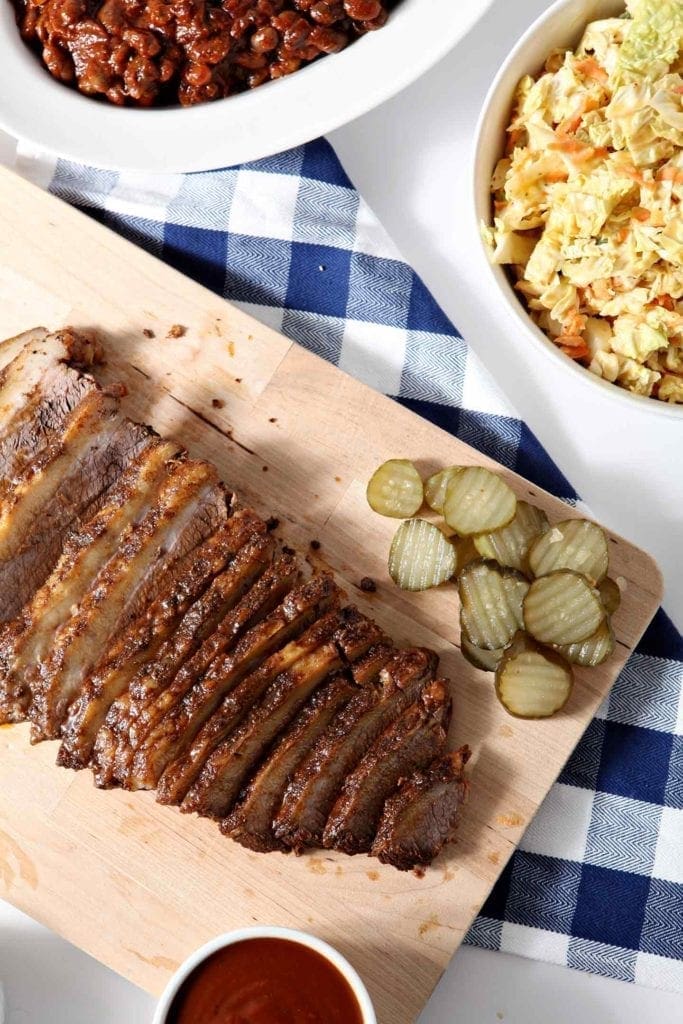 Overhead image of Instant Pot BBQ Brisket, served on a wooden platter with pickles, and other barbecue sides.