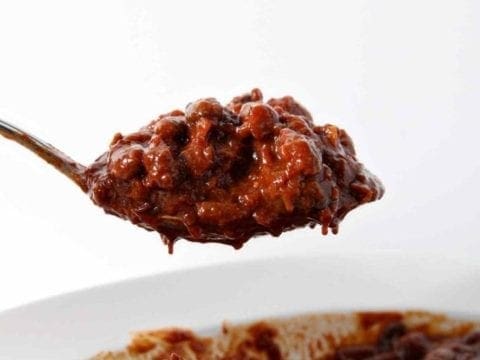 A spoon scoops out a serving of Instant Pot Baked Beans from a white bowl