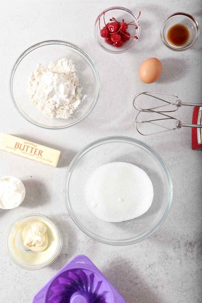 The ingredients for Mini White Chocolate-Cherry Bundt Cakes (Instant Pot Cake) sit on a grey background, ready for putting together