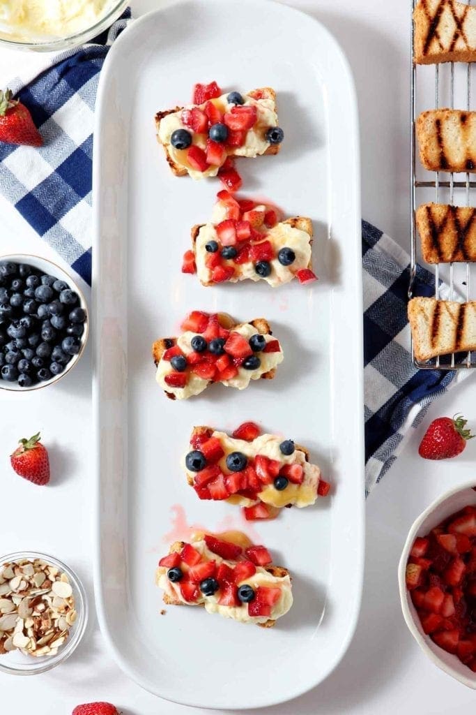 A platter of strawberry bruschetta with almond pudding surrounded by berries