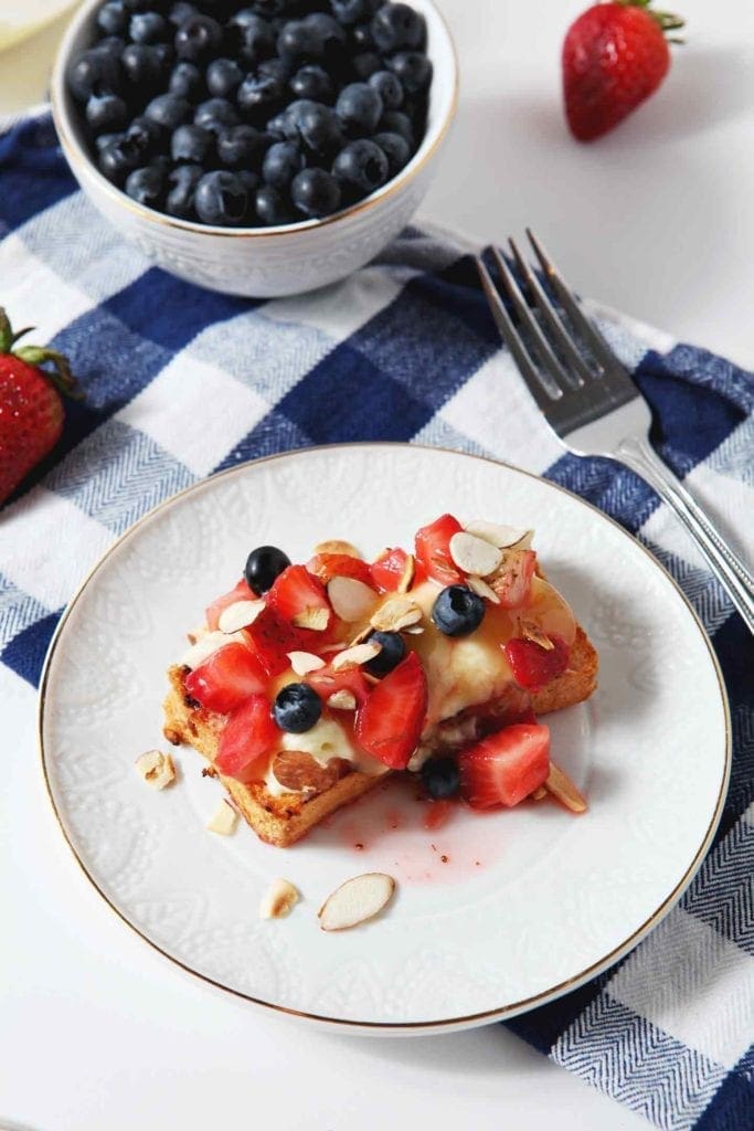 Two slices of grilled angel food cake with pudding and berries on a white plate