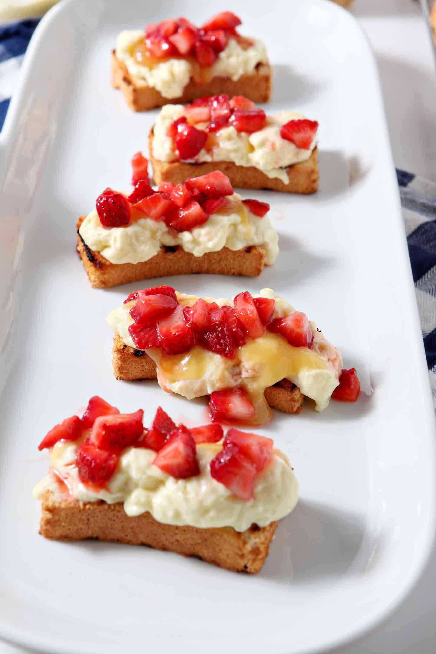 Macerated strawberries are added on top of pudding and lemon curd for the Patriotic Strawberry Bruschetta, shown on a white platter