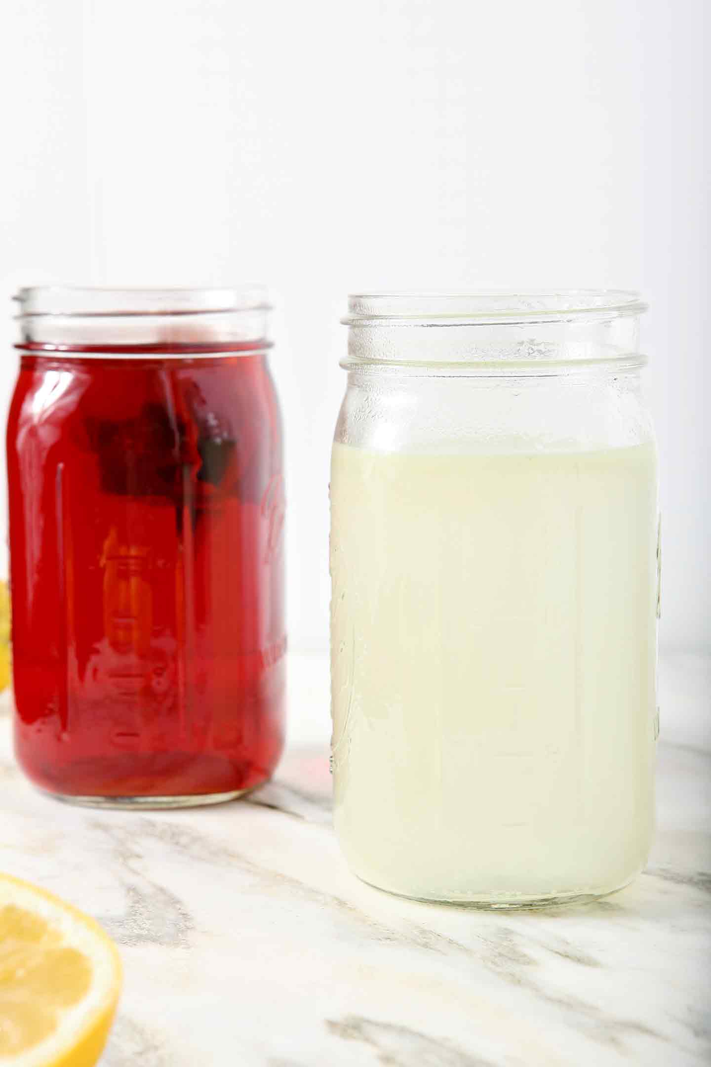 A mason jar full of homemade lemonade and a mason jar full of homemade unsweetened tea sit side by site on a marble background