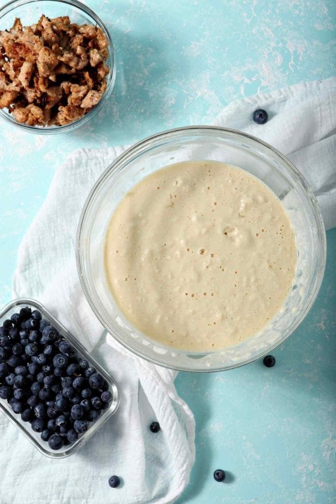 A bowl of pancake batter next to cooked sausage and blueberries