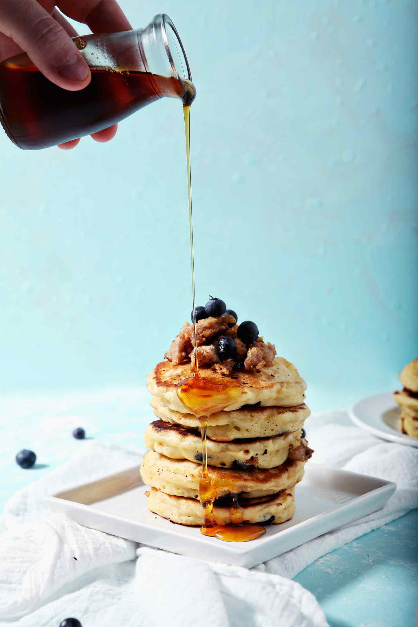 Maple syrup pours on top of Blueberry Breakfast Sausage Pancakes.