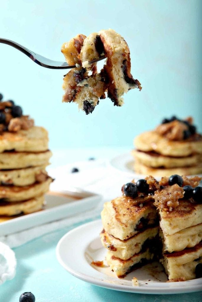 A fork holds a slice of several pancakes with blueberries and sausage