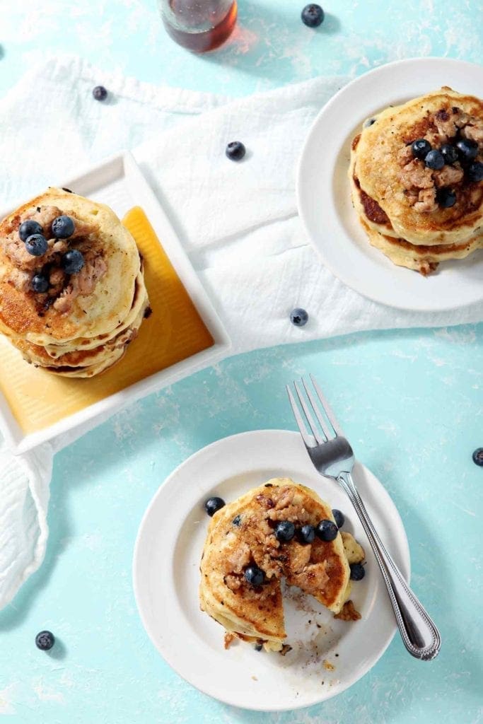 Three plates of Blueberry Breakfast Sausage Pancakes are shown on an aqua background