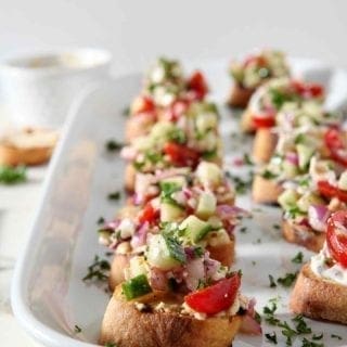 Greek Bruschetta sit on a white platter at a party before serving