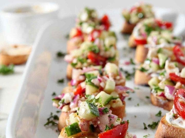 Greek Bruschetta sit on a white platter at a party before serving