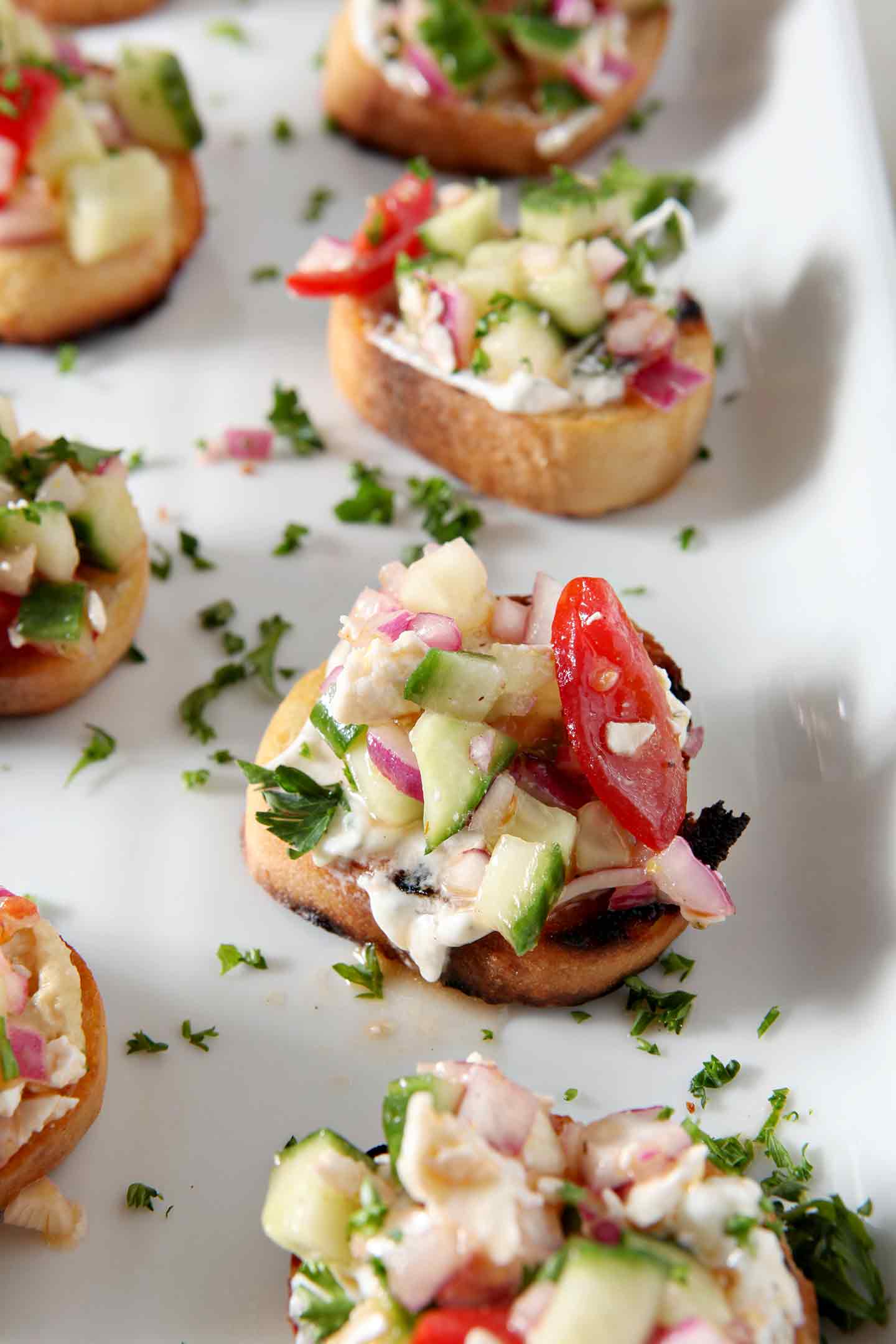 A close up image of the final Greek Bruschetta, garnished with parsley and served on a white platter