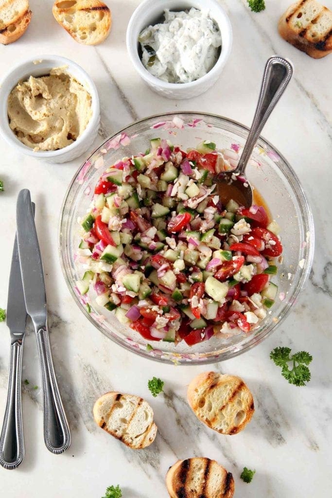 greek bruschetta in a glass mixing bowl with a silver spoon