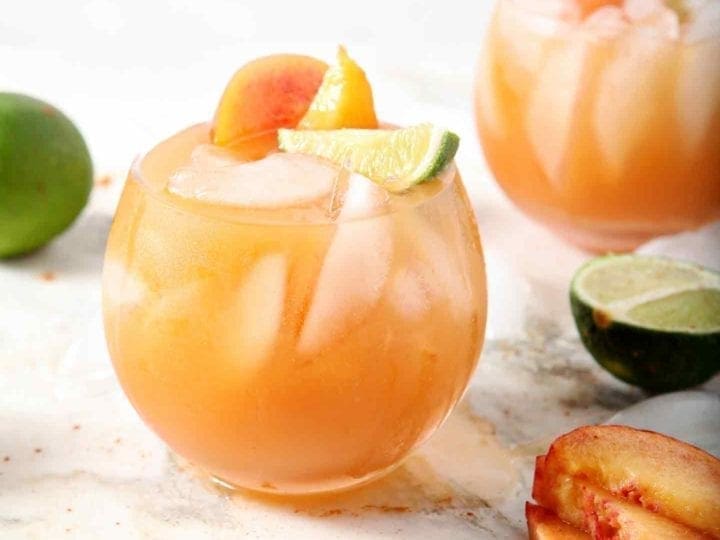 Two Peach Moscow Mule sit on a marble background, surrounded by peach slices and limes