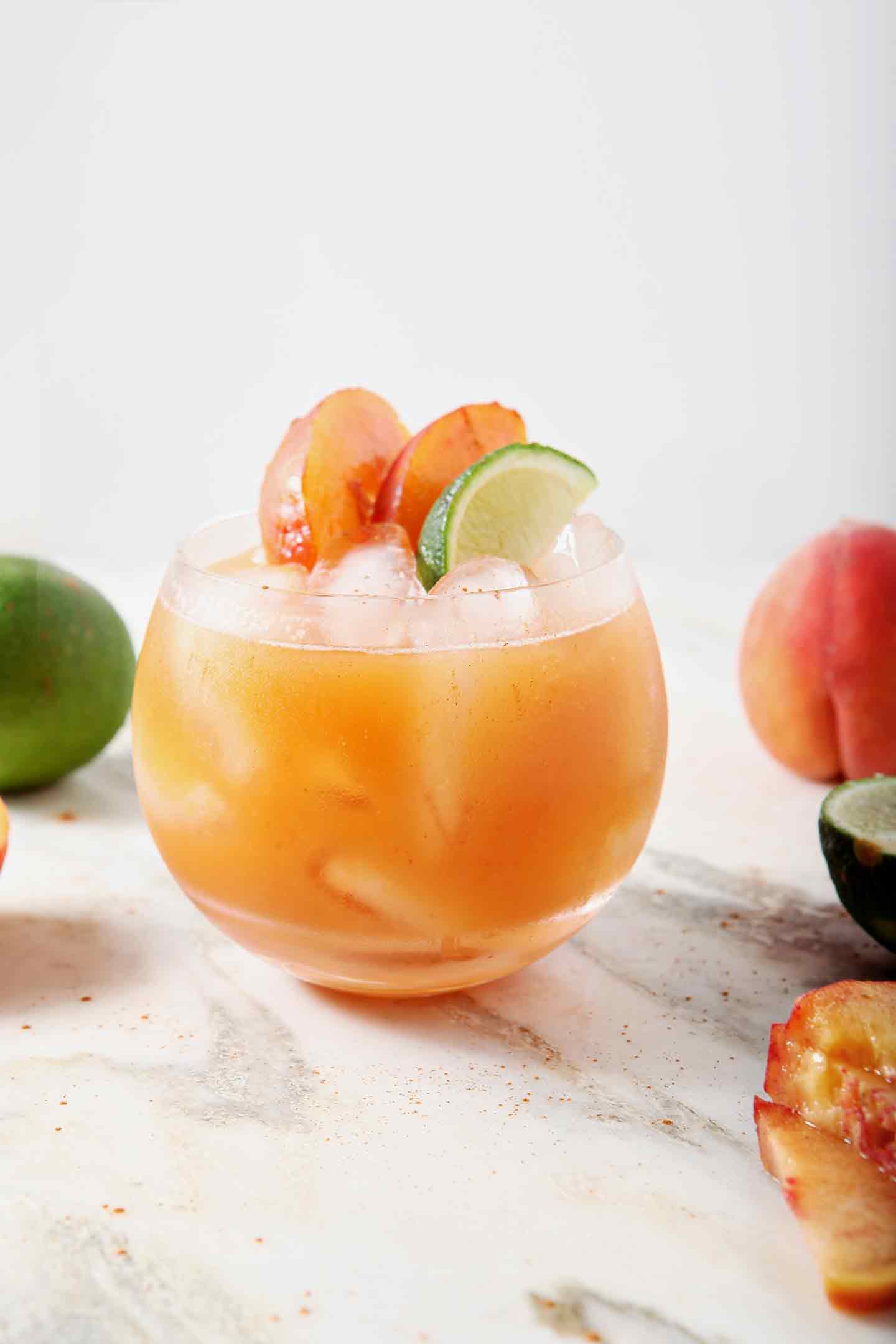 A lone Peach Moscow Mule sits on a marble background, surrounded by peaches and limes