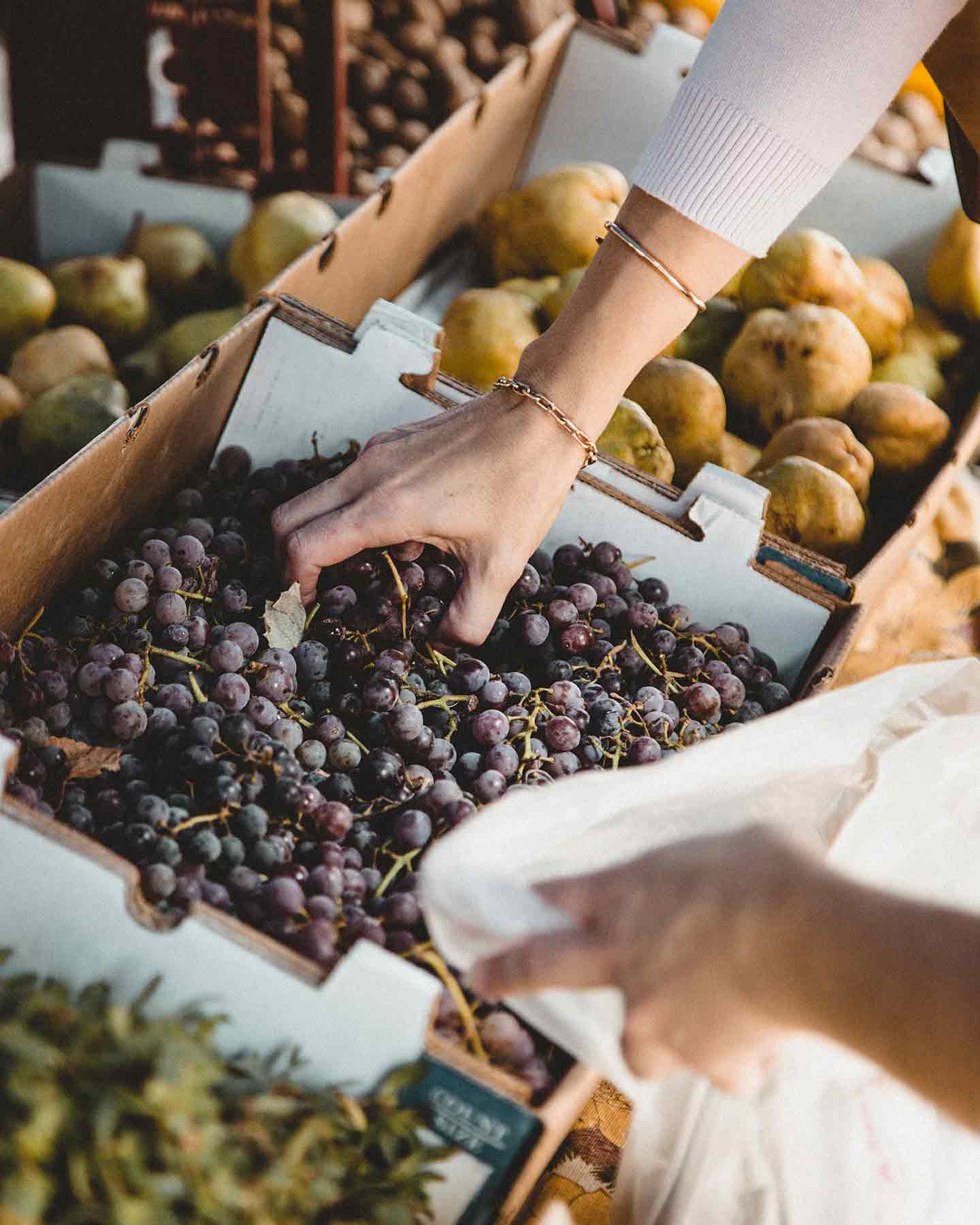 A woman grabs a handful of grapes at a market