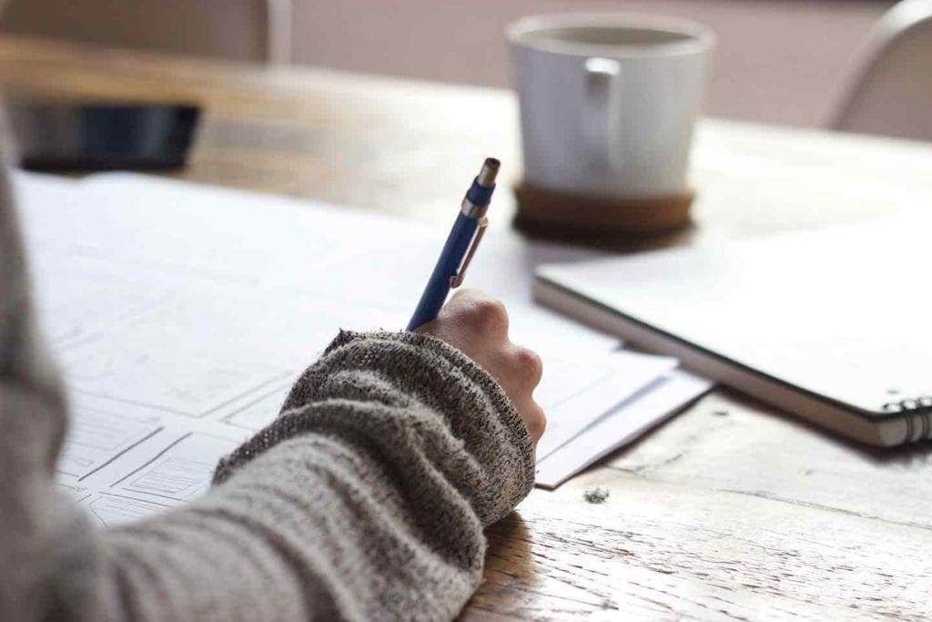 A woman writes a list with papers spread out before her