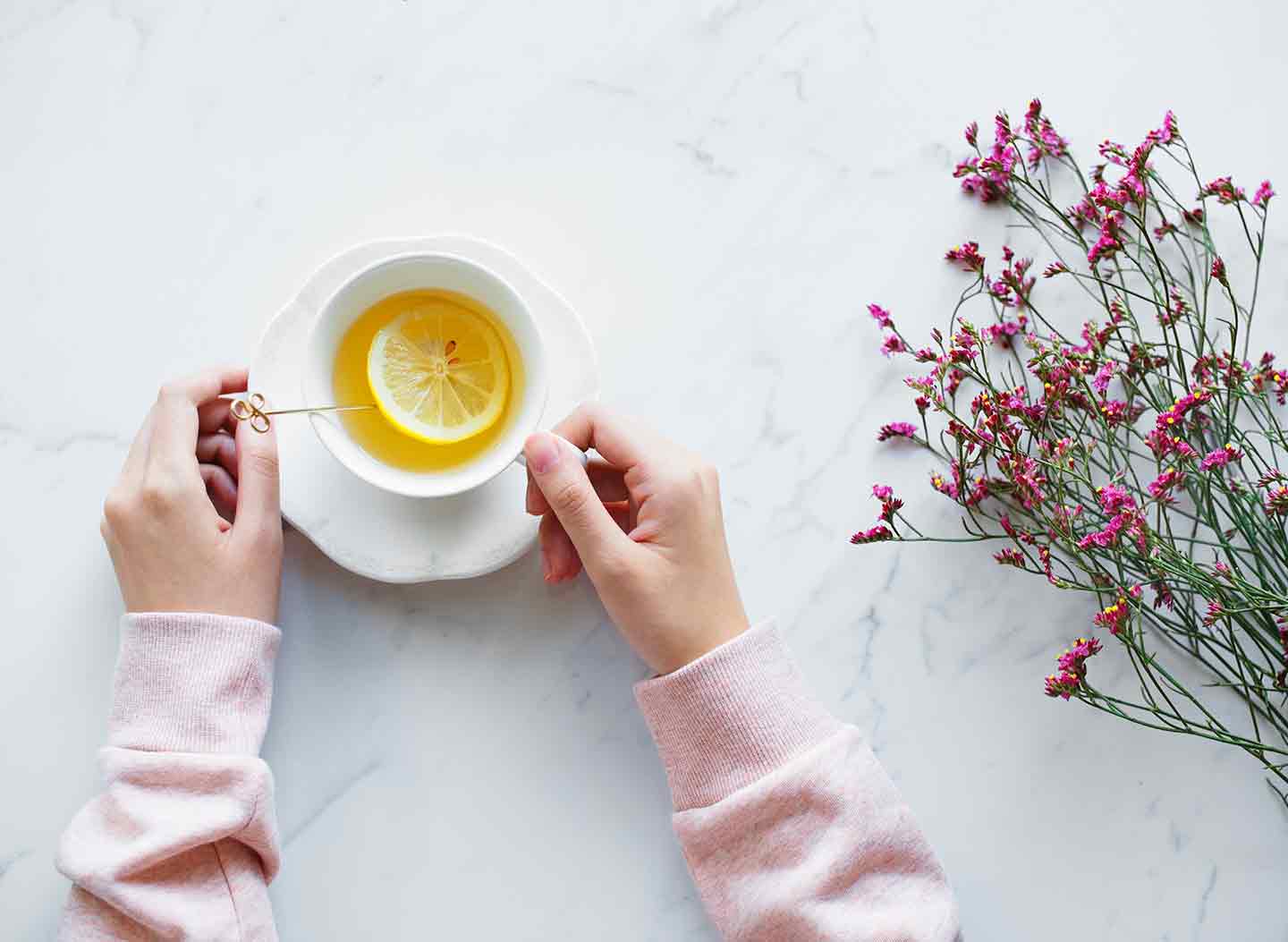 A woman in a pink sweater holds a glass of tea on a marble surface