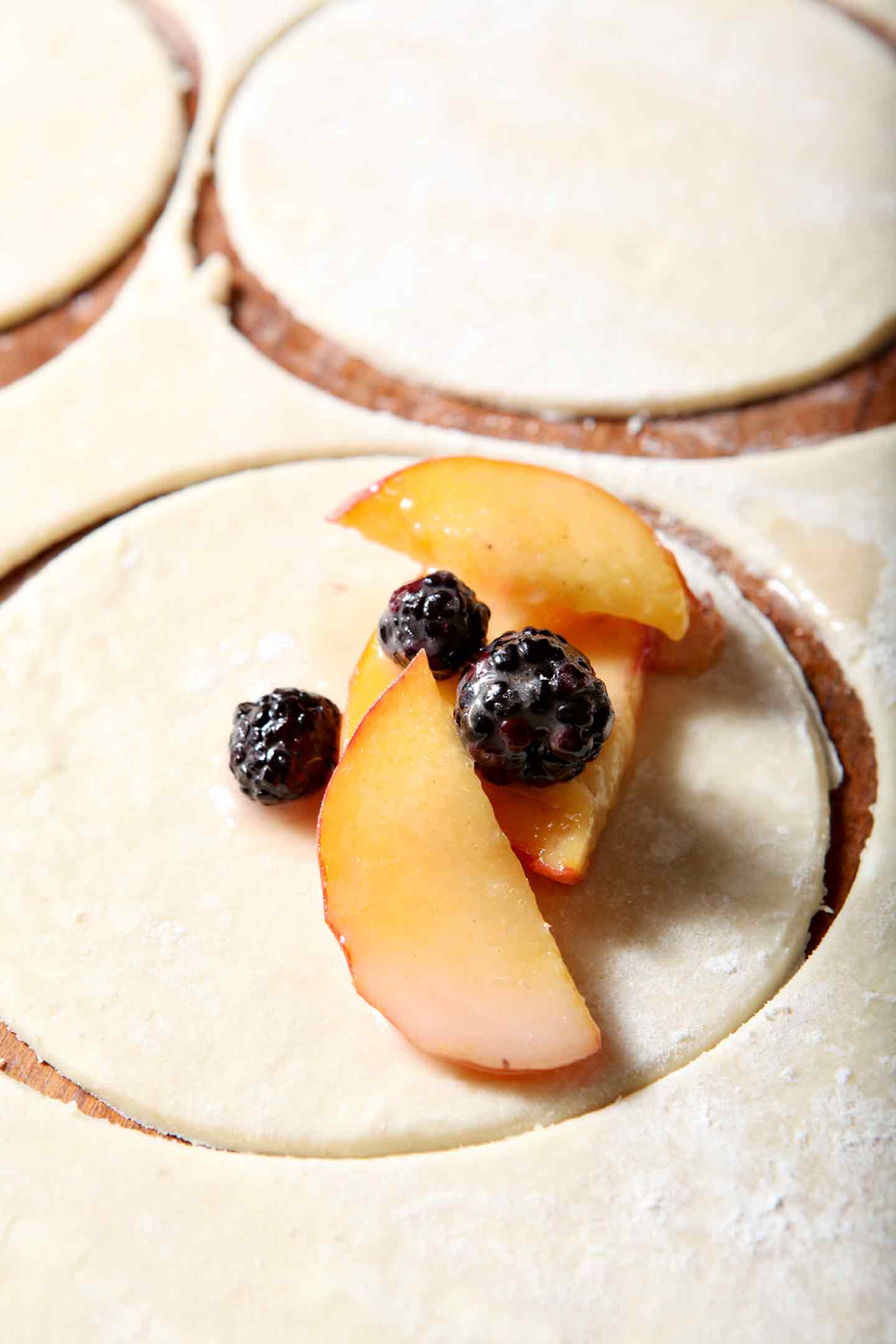 Sliced peaches and blackberries are placed in a pie crust round