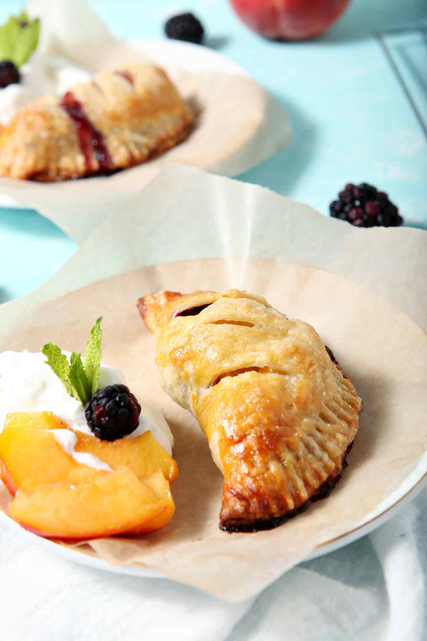 A Blackberry Peach Hand Pie sits on a plate with Bourbon Whipped Cream, peach slices and blackberries