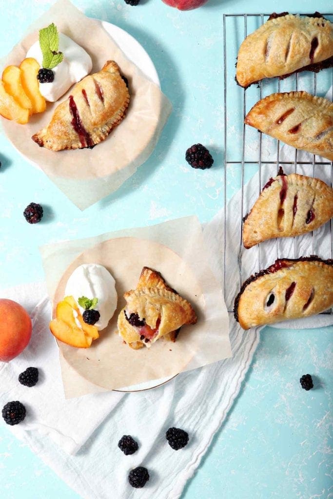 Several Blackberry Peach Hand Pies are served with Bourbon Whipped Cream on an aqua background