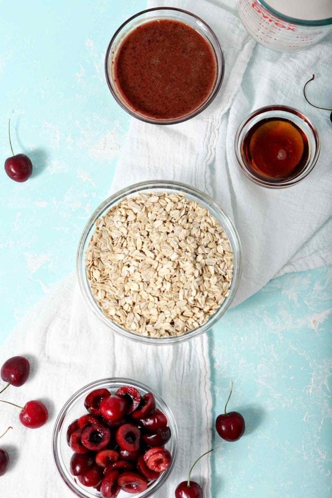 The six ingredients for Cherry Overnight Oats, shown on a turquoise background