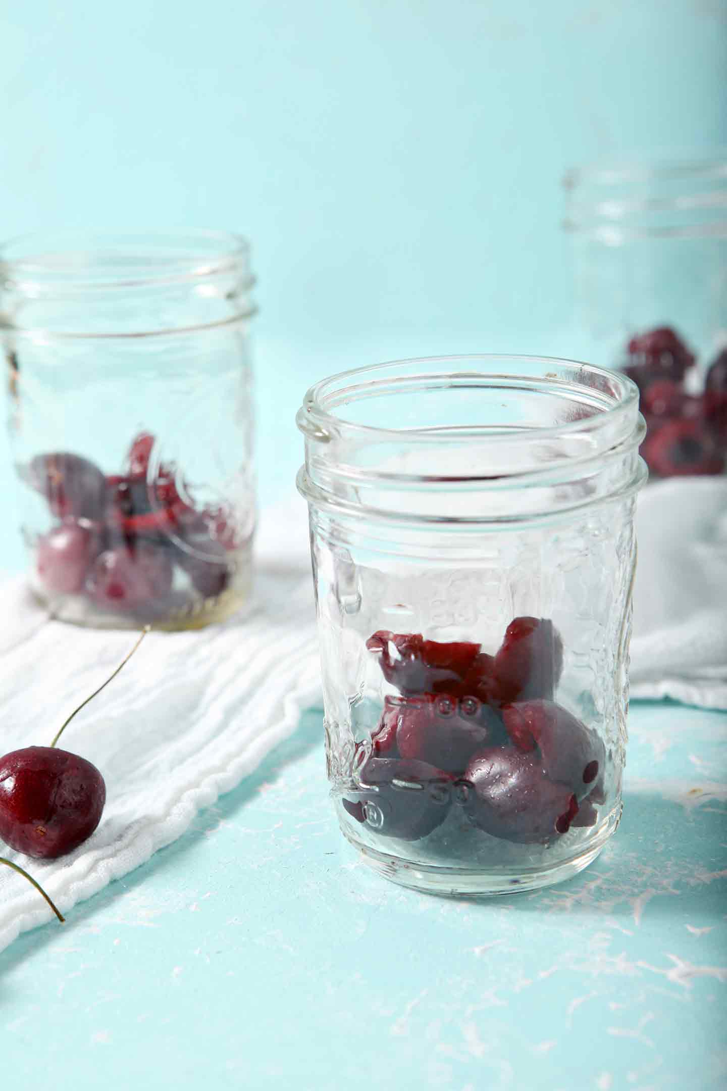 Halved, pitted cherries are shown in the base of mason jars as overnight oats are assembled