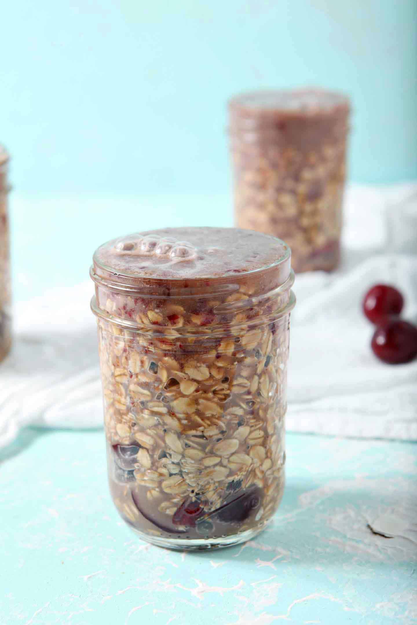 Mason jars of Cherry Overnight Oats are filled to the brim and ready to chill in the refrigerator overnight