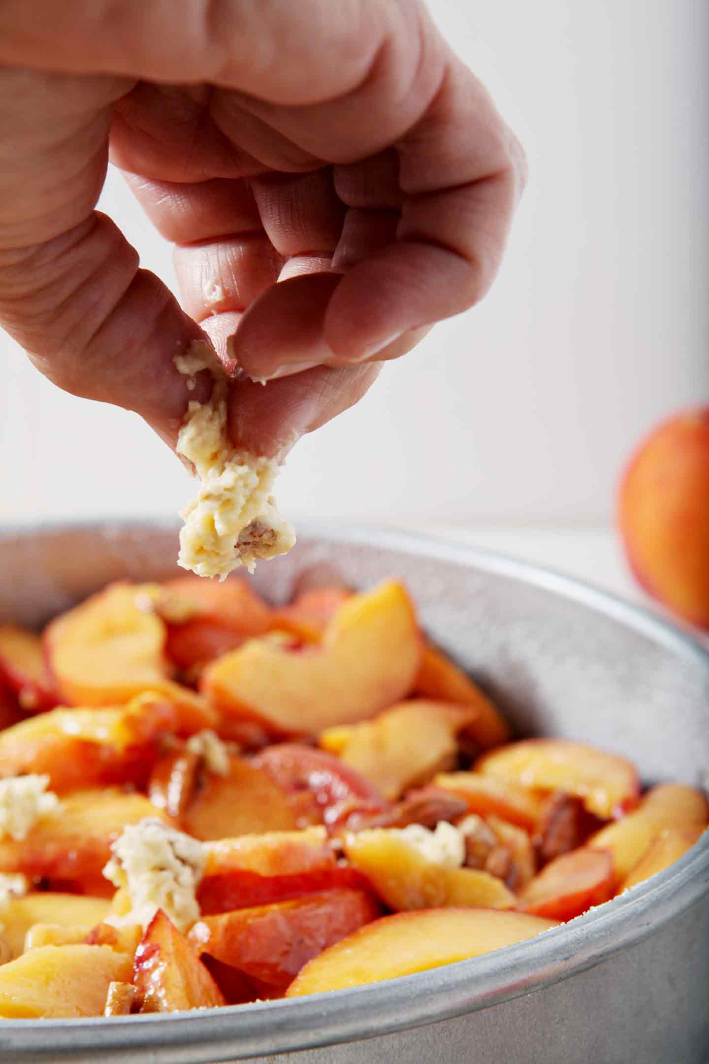 A woman pinches the biscuit topping for Dairy Free Peach Cobbler on top of the peach filling