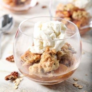 Several servings of Dairy Free Peach Cobbler, topped with dairy free ice cream, sit on a marble background before serving