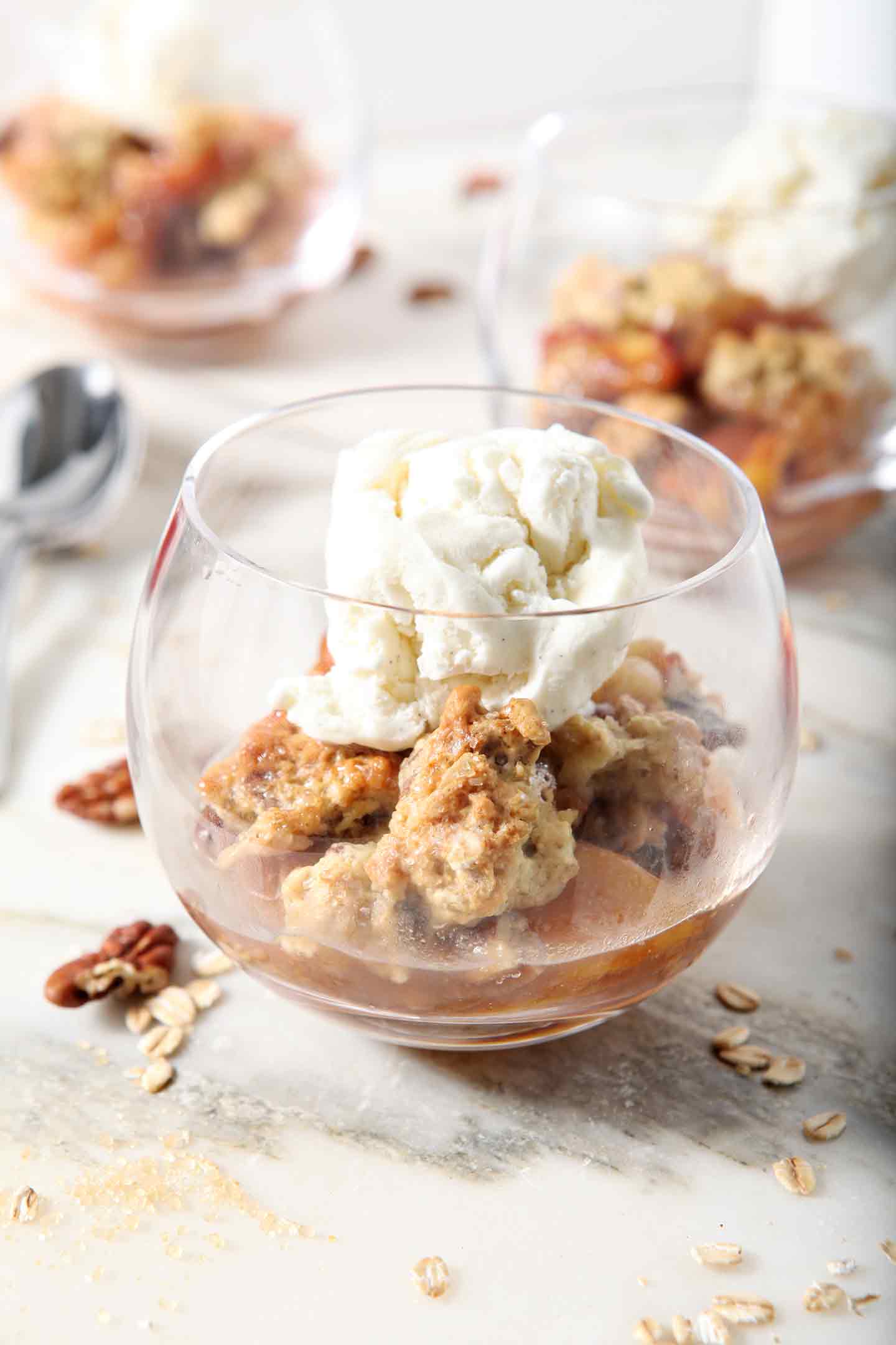 Several servings of Dairy Free Peach Cobbler, topped with dairy free ice cream, sit on a marble background before serving