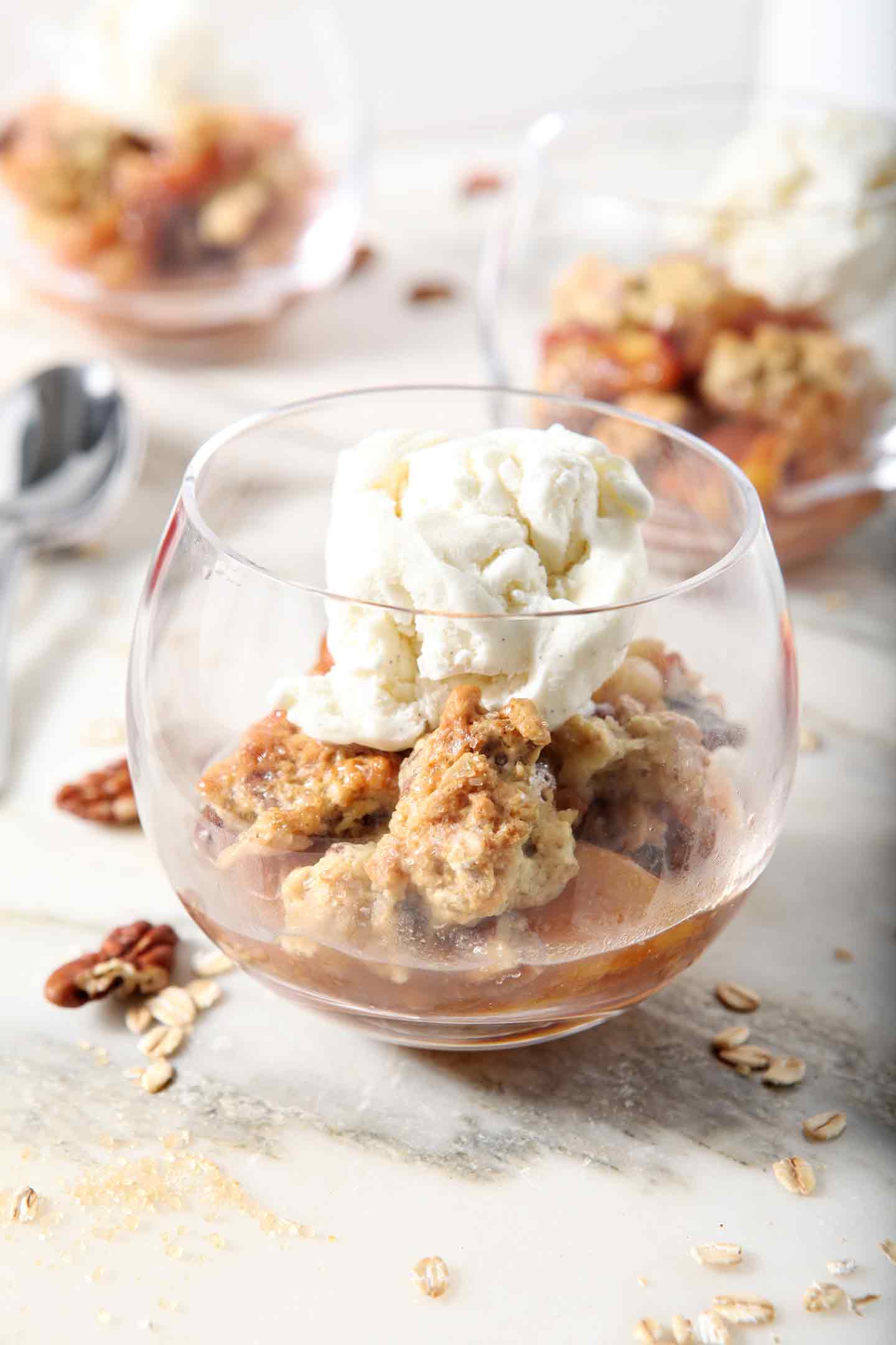 Several servings of Dairy Free Peach Cobbler, topped with dairy free ice cream, sit on a marble background before serving