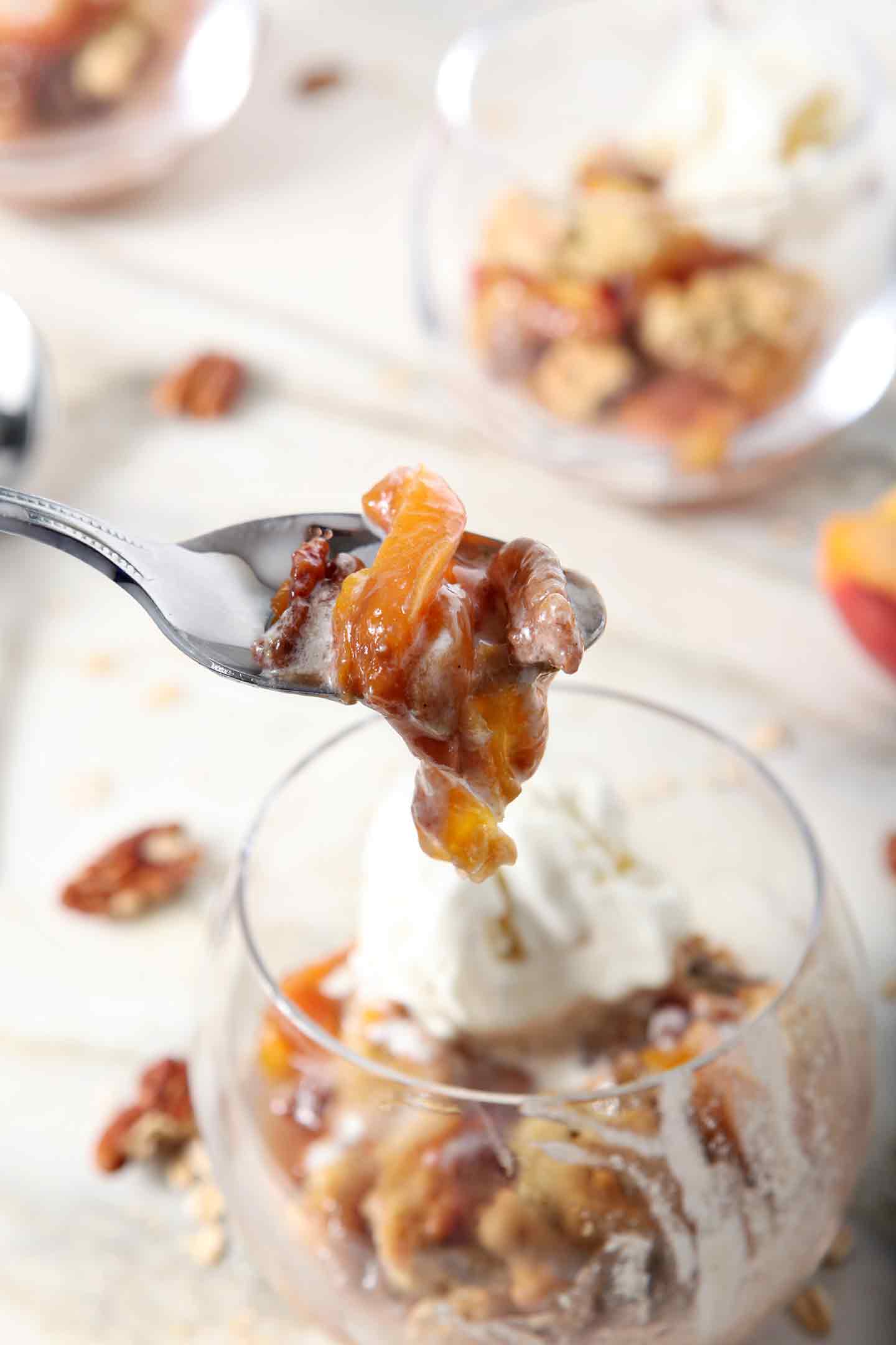 A spoon pulls a bite of Dairy Free Peach Cobbler out of a bowl