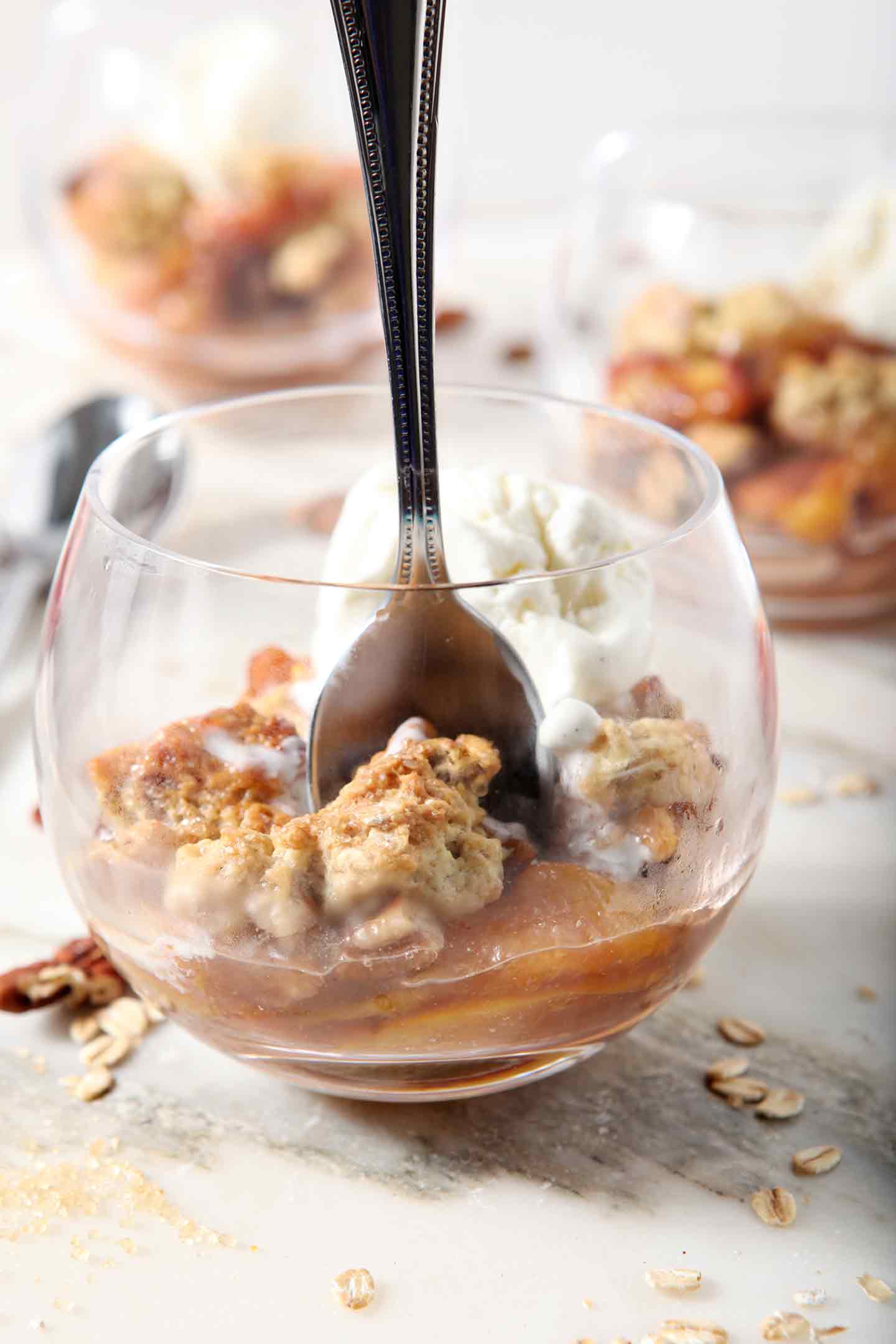 A person digs into a serving of Dairy Free Peach Cobbler, topped with dairy free ice cream, with a spoon