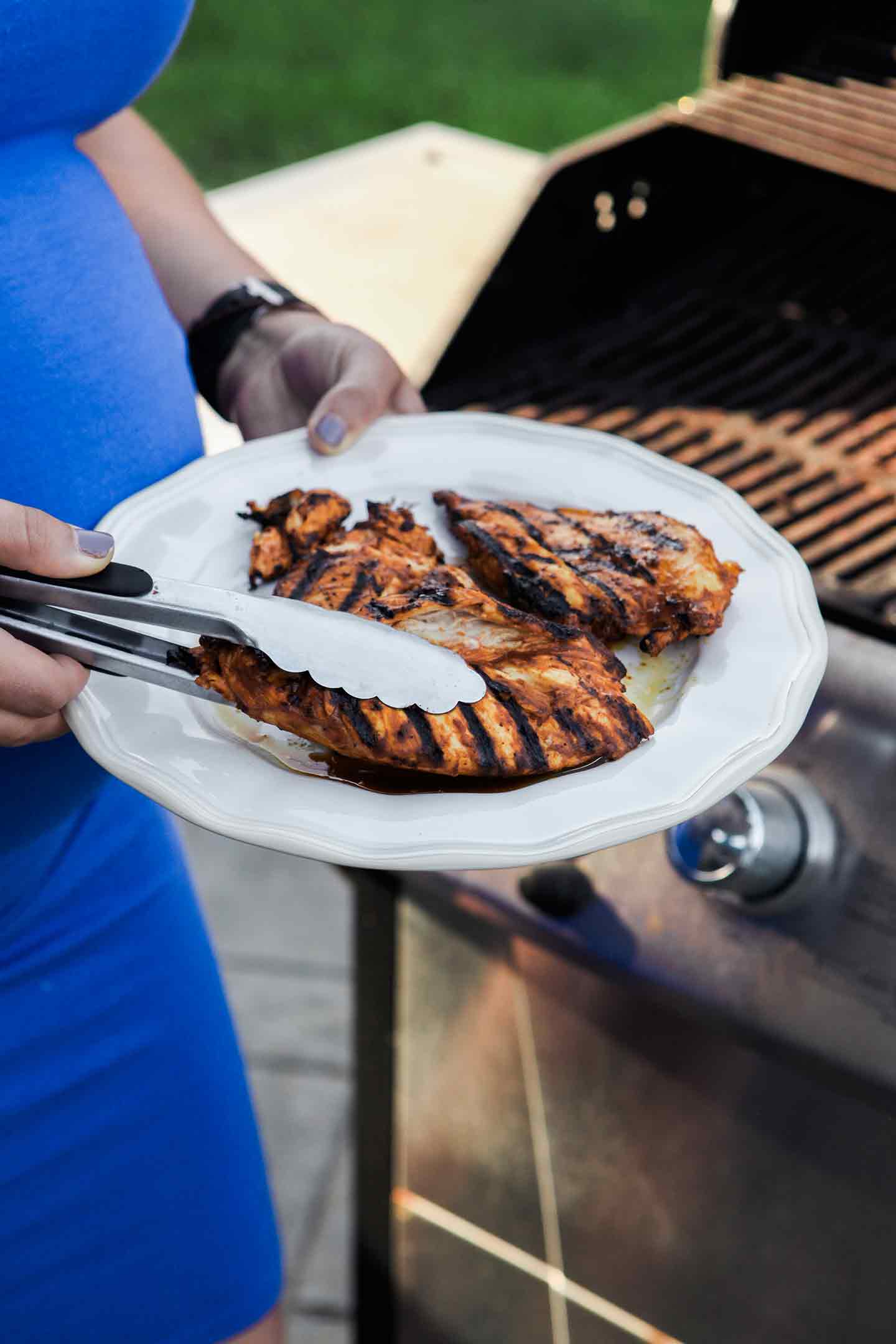 A woman holds barbecue chicken next to the grill