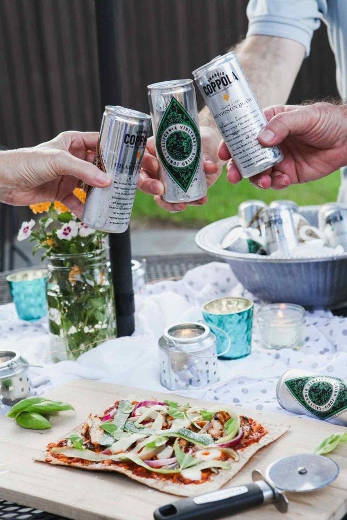 Three people clink Coppola Diamond Collection cans together at an outdoor gathering.