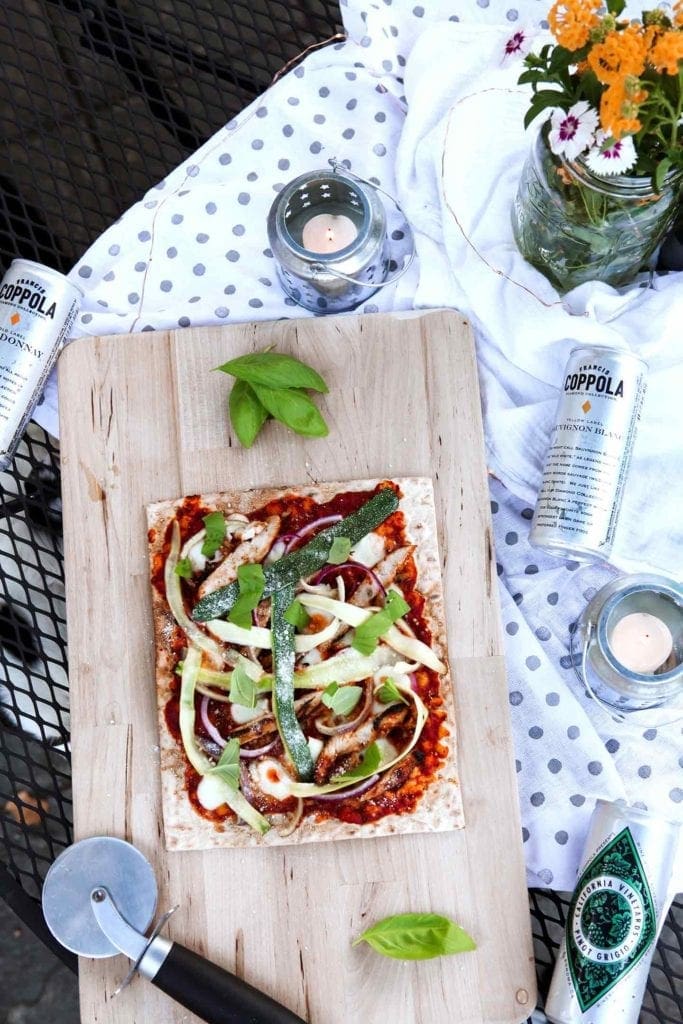 A Grilled BBQ Chicken Flatbread, straight off the grill, sits on an outdoor table, ready for serving.