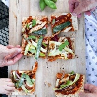 Four people grab for slices of Grilled BBQ Chicken Flatbread, straight off the grill