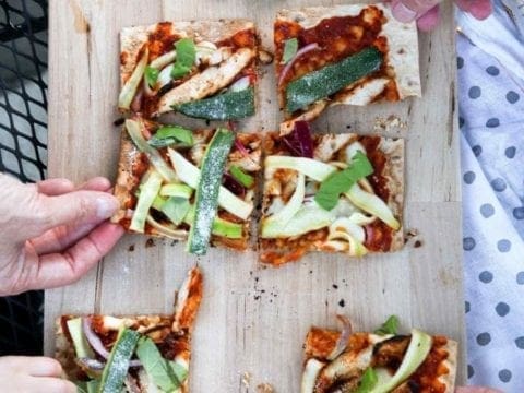 Four people grab for slices of Grilled BBQ Chicken Flatbread, straight off the grill