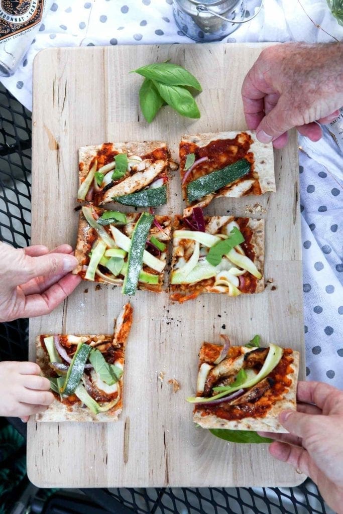 Four people grab for slices of Grilled BBQ Chicken Flatbread, straight off the grill