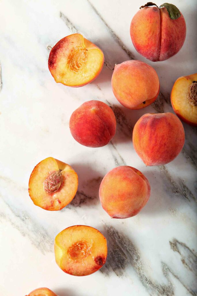 Some whole and some halved peaches on marble