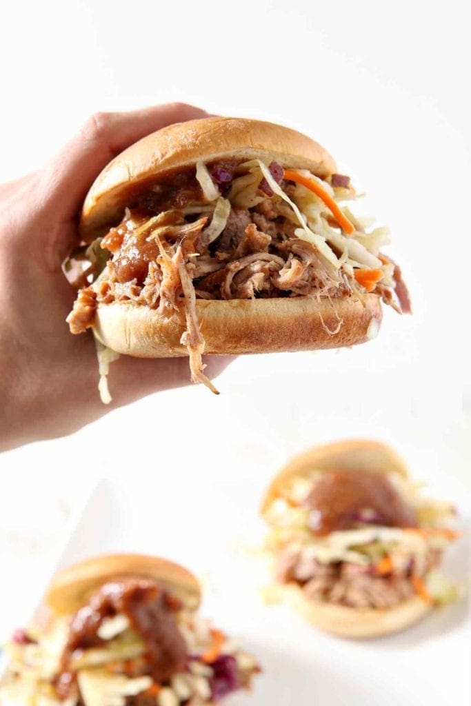 A Pear BBQ Pulled Pork Sandwich is held in hand