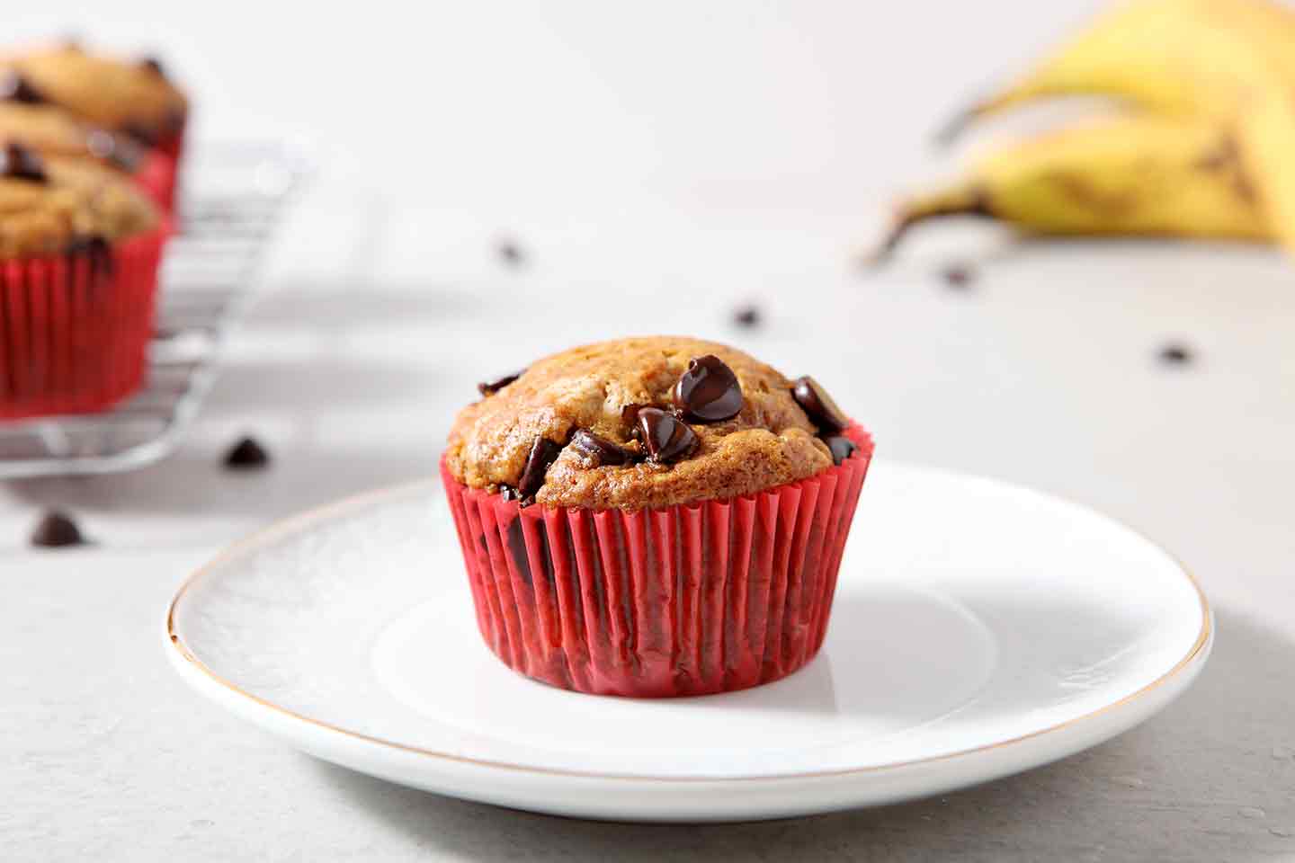 A lone Vegan Banana Chocolate Chip Muffin is placed on a white plate for serving