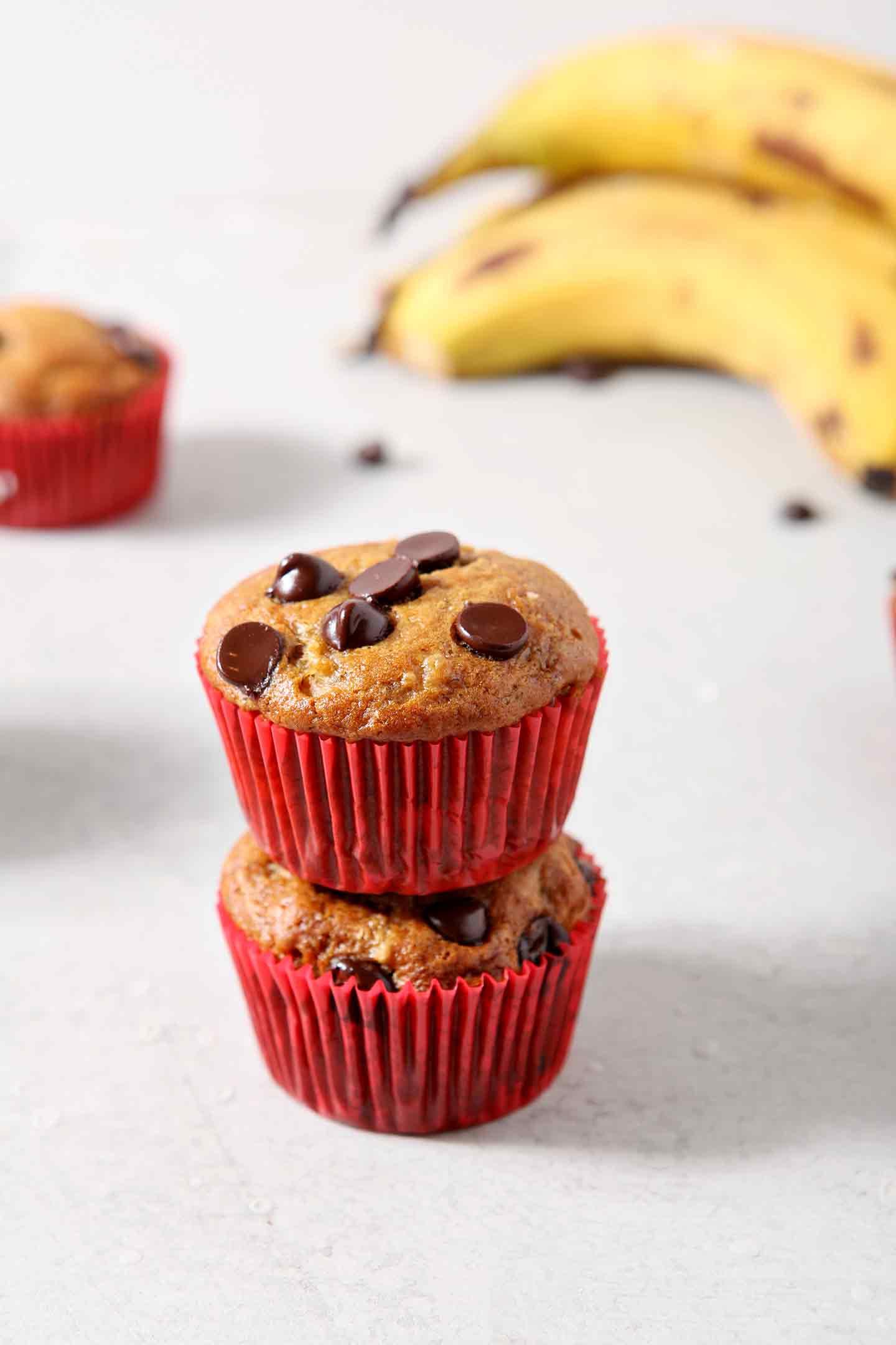 Two Vegan Banana Chocolate Chip Muffins are stacked on top of each other after baking