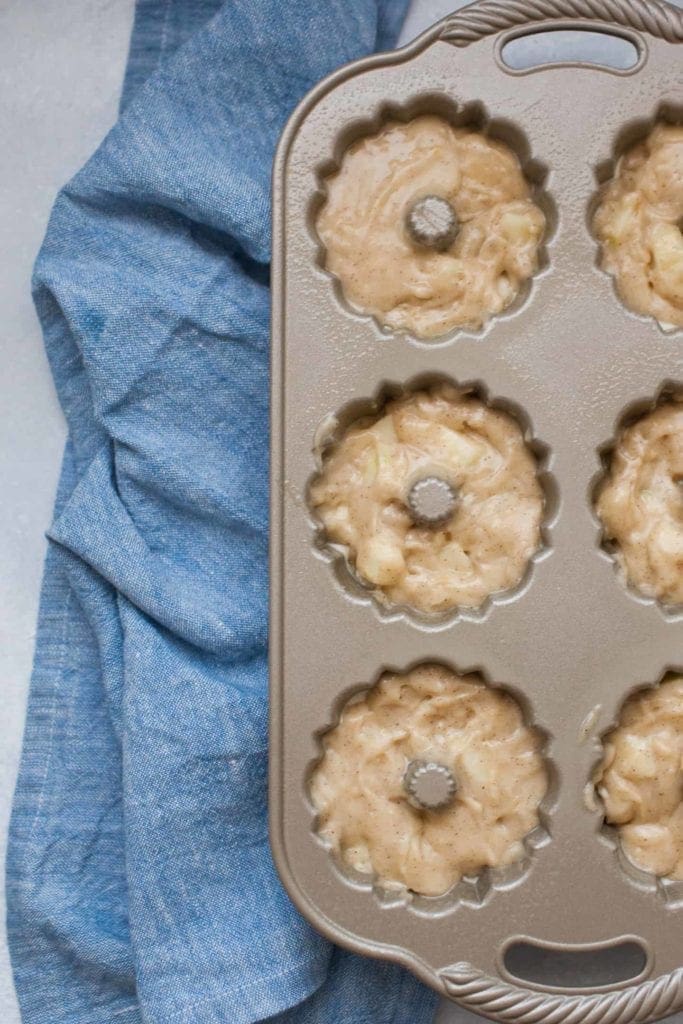 Mini bundt loaf pan on top of a blue chambray napkin, with spiced cake batter in the pan.