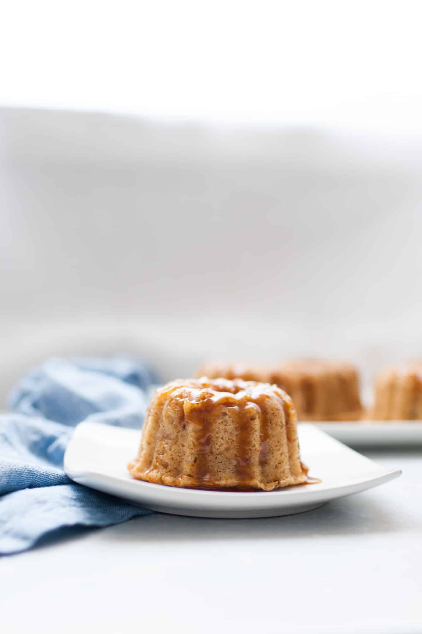 Mini bundt shaped cakes sitting on a white serving platter with small jar of caramel in the background.