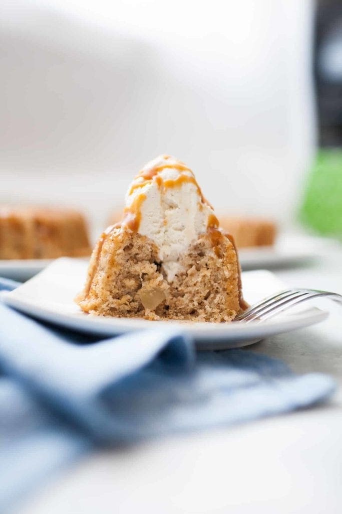 Mini spice cake that has had a bite taken out of it with a fork. Shows the inside of the cake with a scoop of ice cream and caramel drizzled on it.