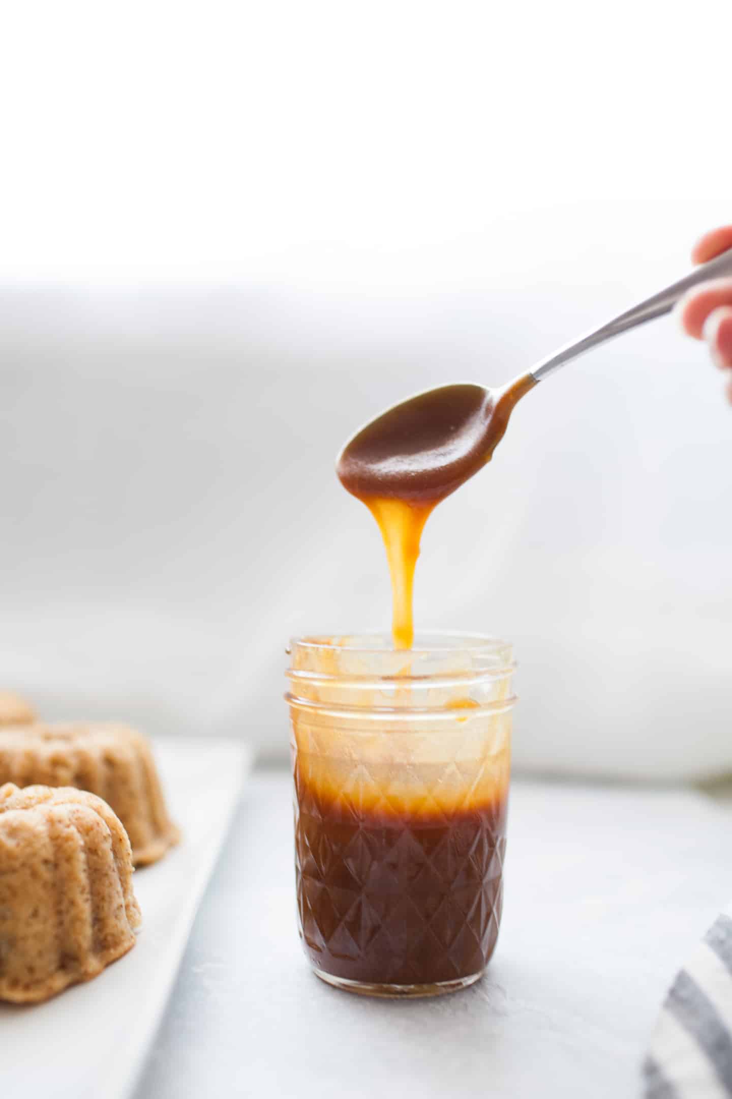 spoon with caramel sauce dripping into a glass jar