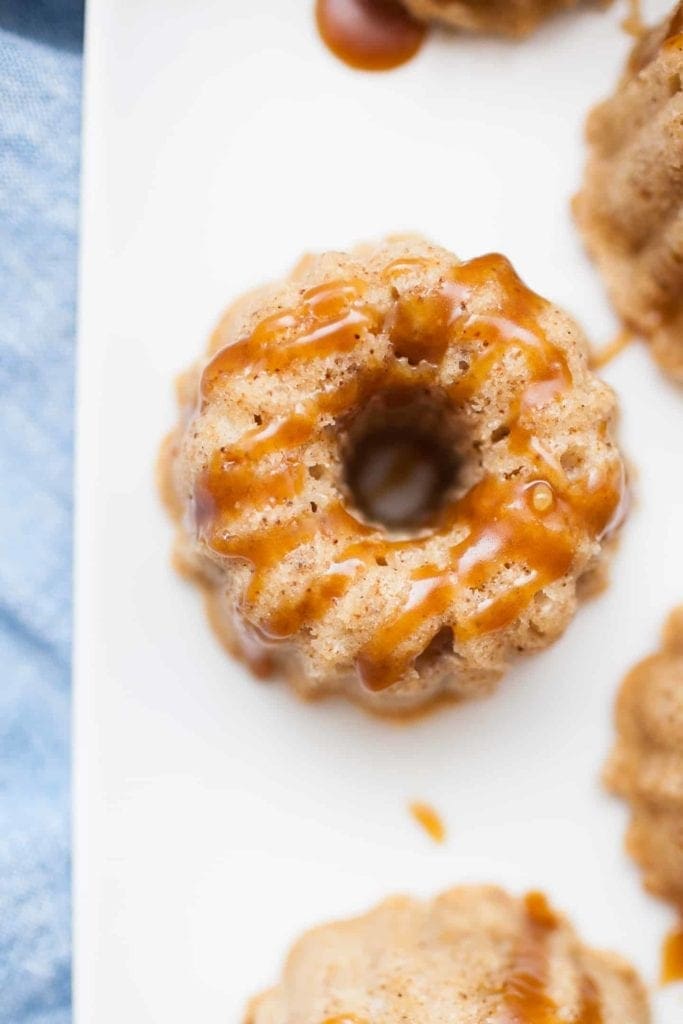 Mini bundt shaped cakes sitting on a white serving platter covered in homemade caramel sauce.