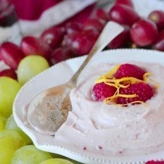 A bowl of Raspberry Yogurt Fruit Dip is served with a spoon and various fruits