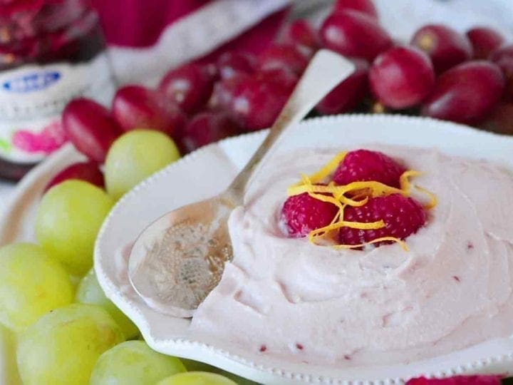 A bowl of Raspberry Yogurt Fruit Dip is served with a spoon and various fruits