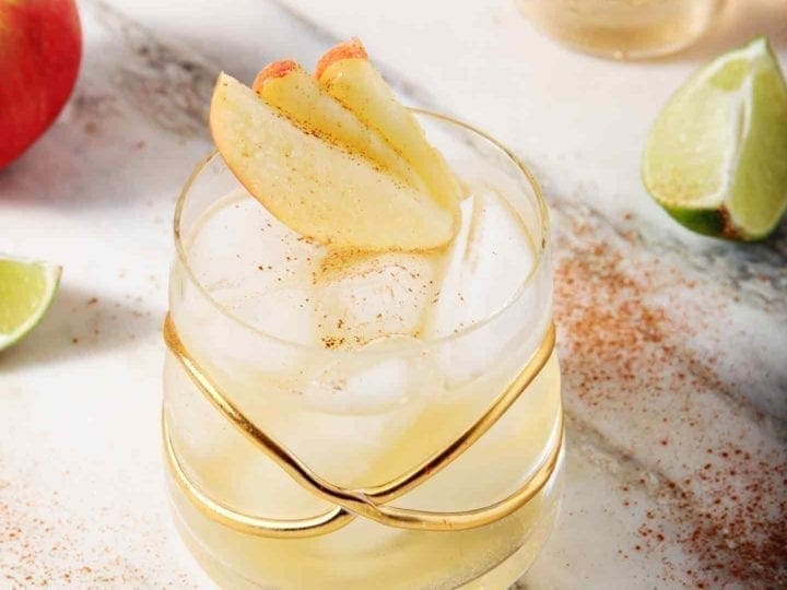 A Apple Pie Moscow Mule sits on a marble background, surrounded by apples and lime slices